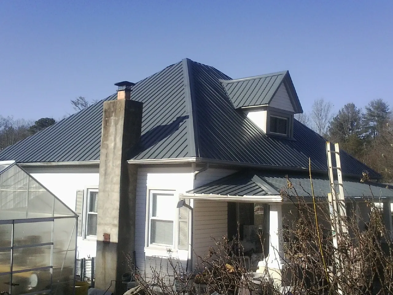 Dark blue standing seam metal roof on a white farmhouse with dormer — Slate & Tile Roof Repair by Roofing Brothers in Lincoln