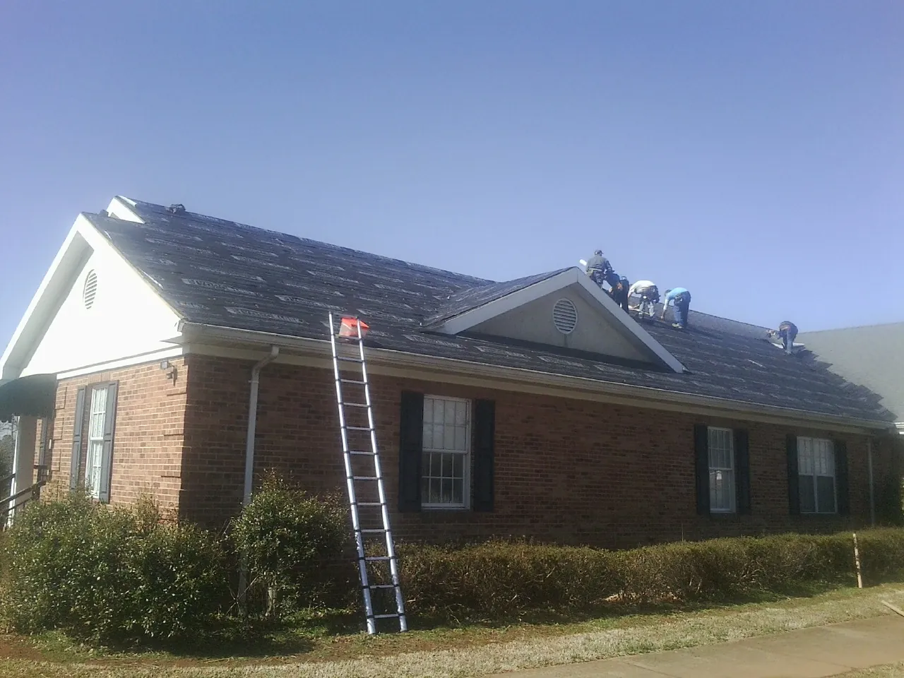 Crew tearing shingles off a brick ranch roof with a ladder set — Metal Roof Repair work by our crew in Lincoln